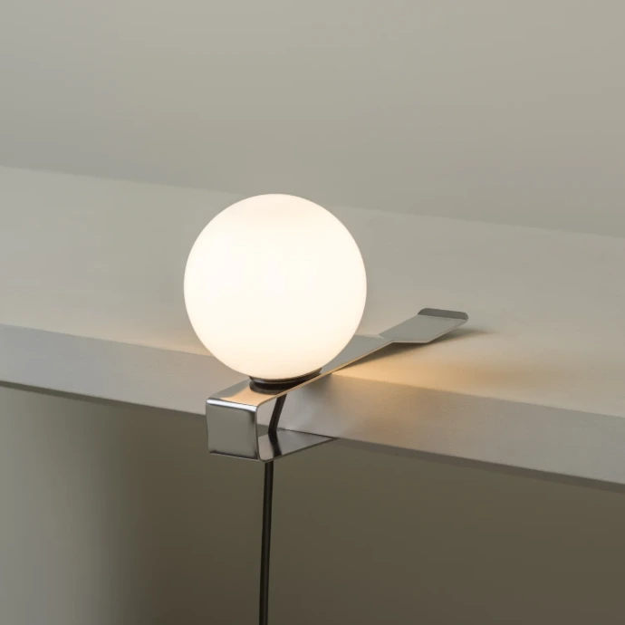 MILAN Klemmleuchte GRIP aus verchromtem Federstahl mit opalweissem Glasdiffusor auf Regalbrett aufgesteckt.
