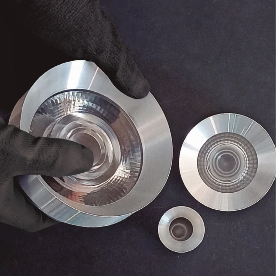 Drei HERLIGHTING Drehteile aus rohem Aluminium mit Hand in schwarzem Gummihandschuh